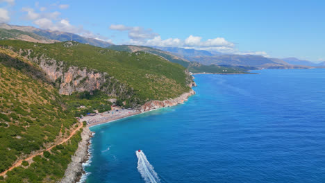 aerial drone tilt down shot over mountain slope along seaside with gjipe beach in distance in albania on a cloudy day