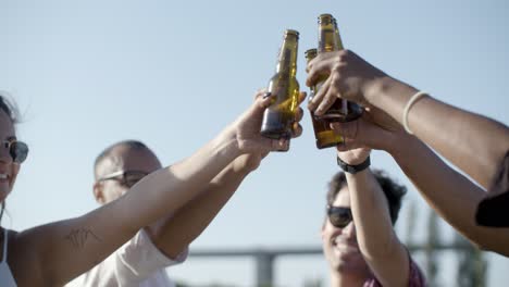 cheerful young people cheering with beer bottles in park.