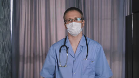 médico en uniforme azul con estetoscopio se pone una máscara facial