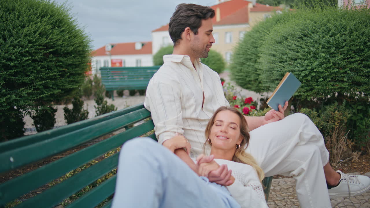 사랑하는 커플이 공원 벤치에서 평온을 즐기고 있습니다. 소설을 읽는 부드러운 남자