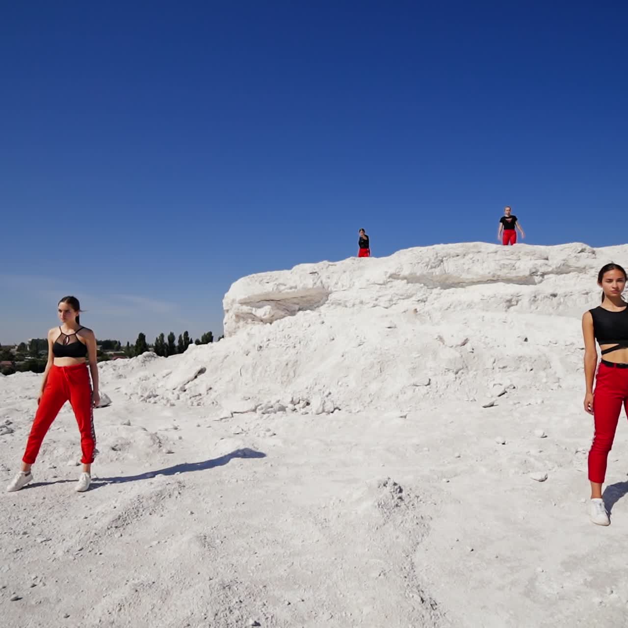Group of teenage girls standing in distance from each other making moves. Dance group performing on the white rocky ground on sunny day