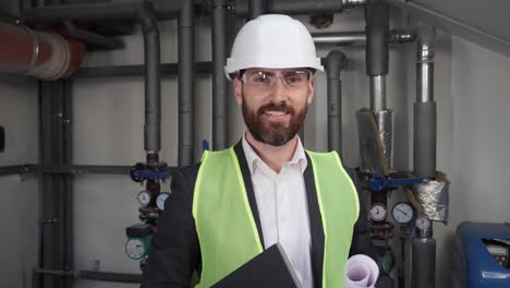 portrait of smiling talented male architect holding blueprint standing near water supply systems. busy concentrated adult man engineer looking at camera positive. engineering design boiler house.