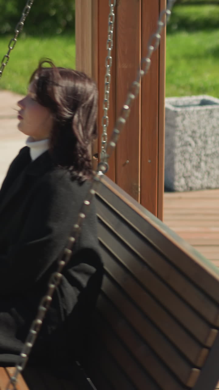 primer plano de una mujer sentada en un columpio de madera, su cabello soplando suavemente en el viento, rodeada de exuberante vegetación en un entorno de parque sereno