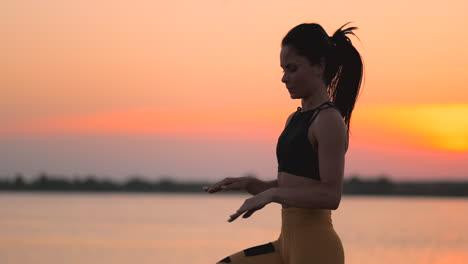 woman trains running on the spot at sunset on the beach near the pond. training at dawn