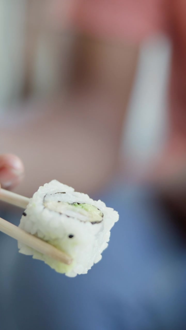 Henkilö pitelee sushipalaa syömäpuikoilla