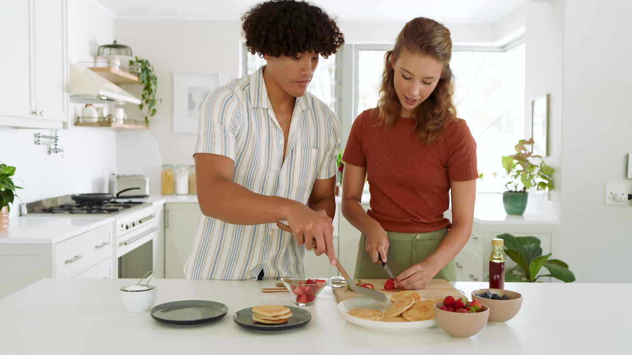 Diverse couple preparing fresh fruit together in modern kitchen, enjoying cooking time, at home