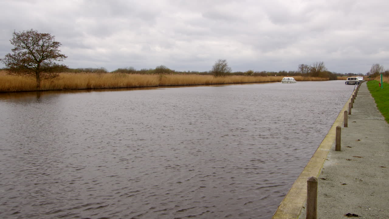 Billede der ser op ad floden Bure med en hvid Norfolk Broads turbåd, der passerer fortøjede både