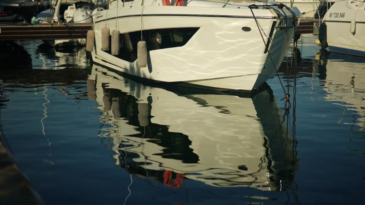 Nahaufnahme eines weißen Yachtbugs mit Fendern und Festmacherleinen, wunderschön gespiegelt im ruhigen Hafenwasser, Antibes, Frankreich
