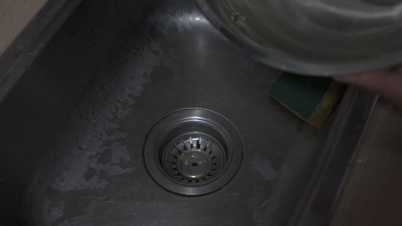 Dirty water being poured to sink after cleaning and preparing vegetables close-up shot