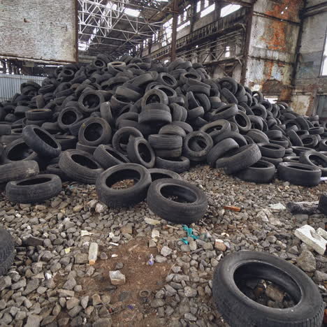 many waste rubber tires lying on the ground inside the old factory. big pile of used black car wheels on the empty territory. camera moves bottom up