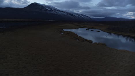 Lappland-sweden-swamp-lake-and-forested-mountain-rivers-below-snowy-mountain-at-blue-hour