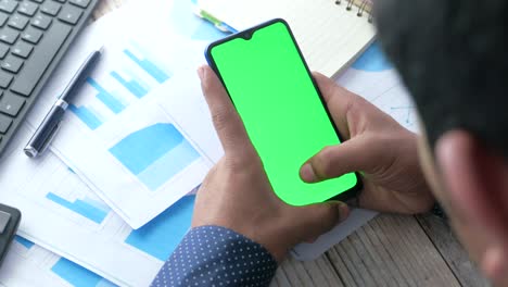 person using smartphone with green screen over business documents