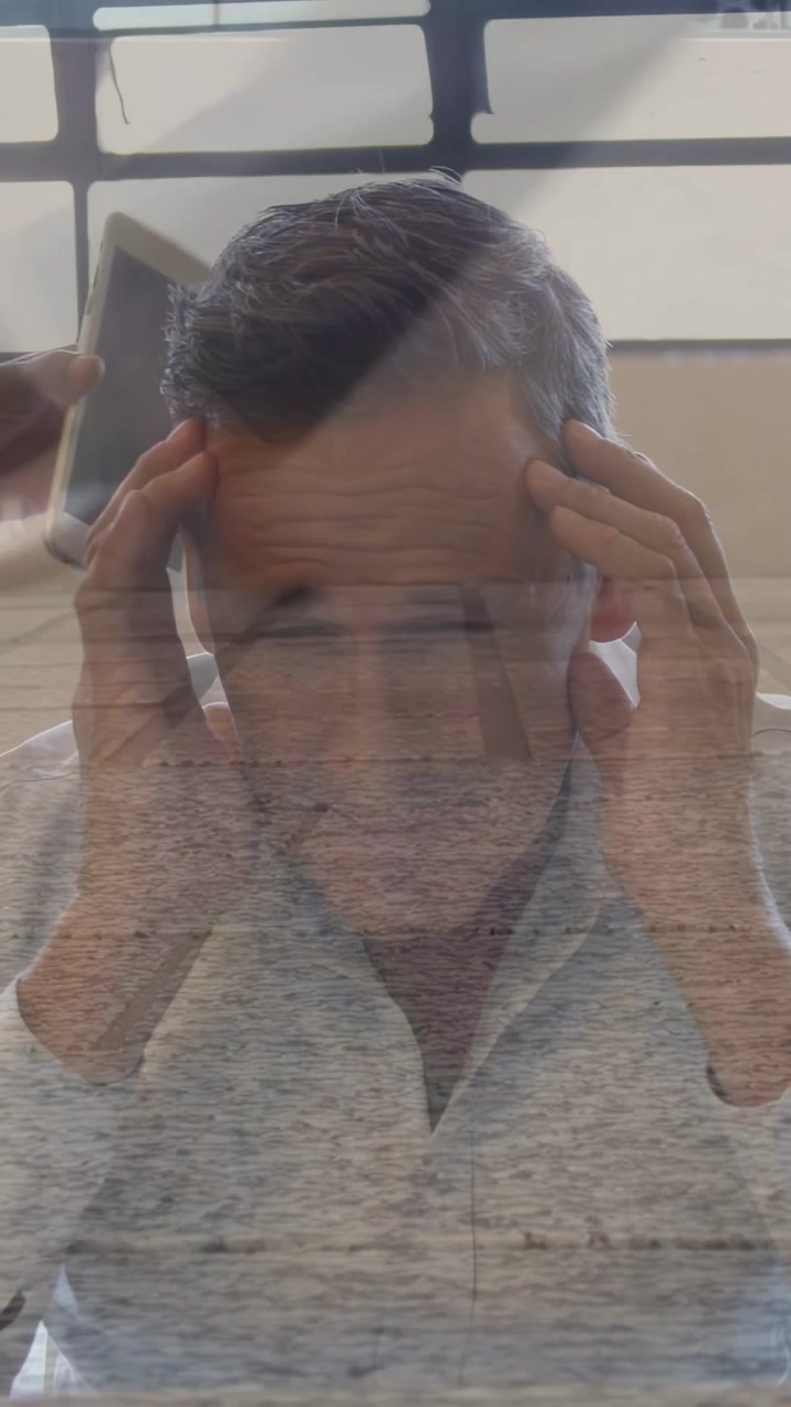 Homem reagindo a um ajudante segurando um smartphone perto da orelha, pressionando as têmporas enquanto realiza um teste de audição.