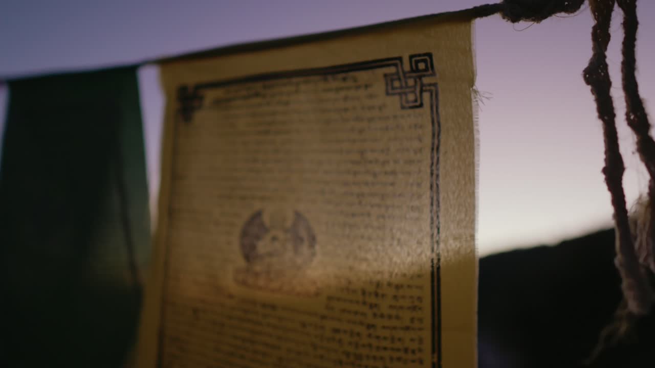 Prayer flag with text and symbols, gently waving against a twilight sky
