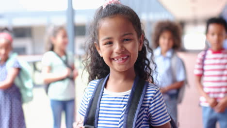 smiling girl with backpack in school hallway, standing with classmates