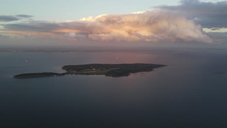 a distant drone footage of an island on sunset with colourfull couds above it