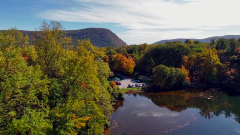 Una-Vista-Aérea-Sobre-Un-Lago-Reflectante,-Rodeado-De-árboles-Coloridos-Durante-El-Follaje-De-Otoño-En-El-Norte-Del-Estado-De-Nueva-York