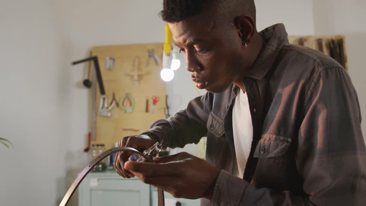 Focused african american craftsman using tool to make a hole in leather workshop