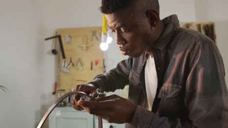 focused african american craftsman using tool to make a hole in leather workshop