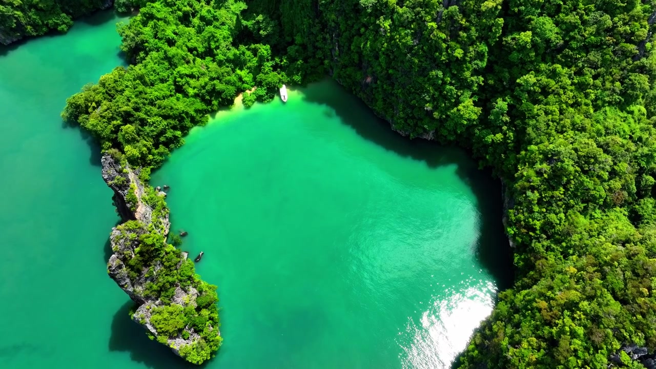 Una piccola barca ormeggiata in acque turchesi circondata da formazioni carsiche calcaree coperte da fitta vegetazione tropicale nel Parco Nazionale Ao Phang Nga. Isola di Ku Du Yai, Phuket, Thailandia.