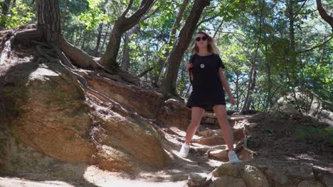 female hiker backpacker wearing black clothes walking down the rocky slope hill in gwanaksan mountain forest in south korea on sunny summer day - from view low angle
