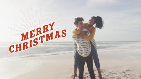 Animation-of-merry-christmas-text-in-red-over-happy-biracial-couple-piggybacking-on-beach