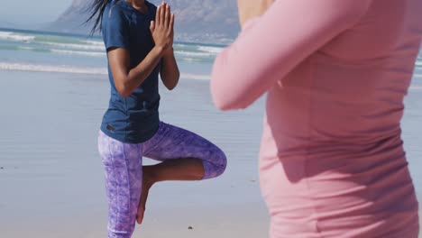 Multi-ethnic-group-of-women-doing-yoga-position-on-the-beach-and-blue-sky-background