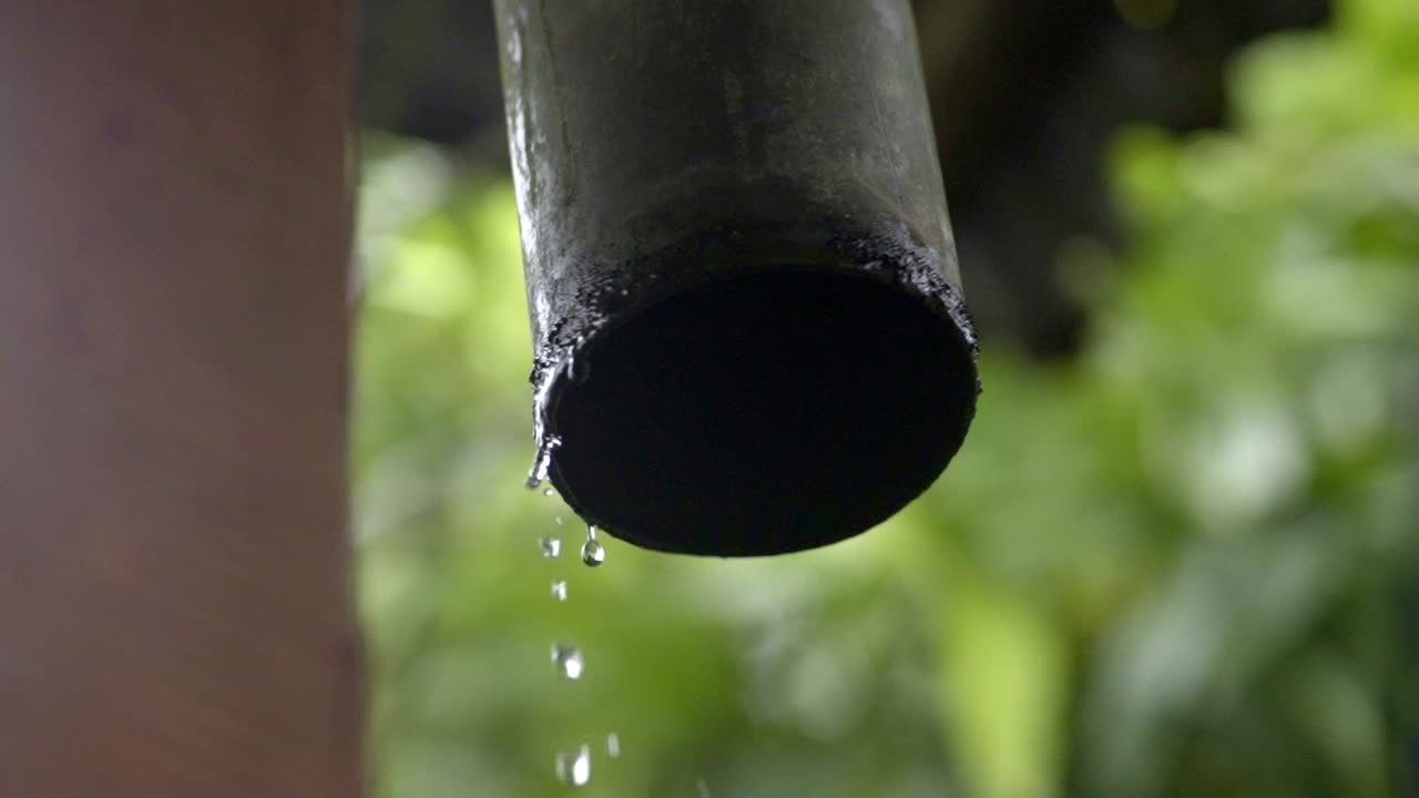 Water pouring out of rain gutter from roof, raindrops out of PVC pipe closeup