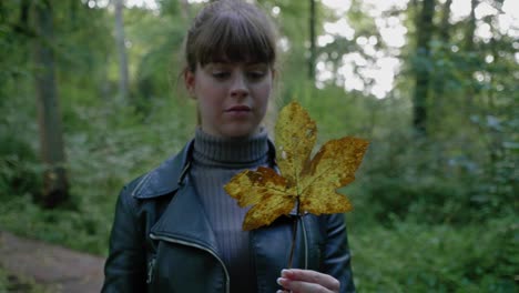 beautiful young woman twirls gold sweatgum leaf in forest, tracking