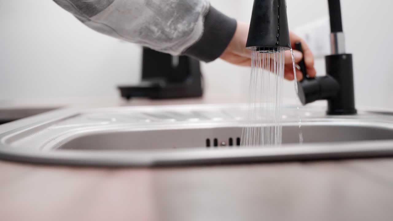 Nærbillede af en person, der tænder og slukker for en moderne vandhane i slow motion.