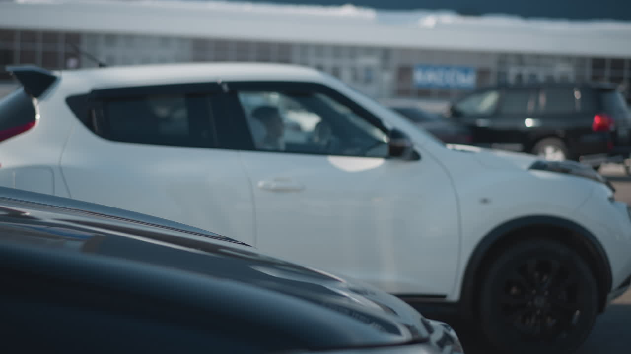 cars parked on both sides of street with vehicles driving along busy urban road, blurred motion, clear daylight, asphalt pavement, building facade in background, winter season with snow accumulation