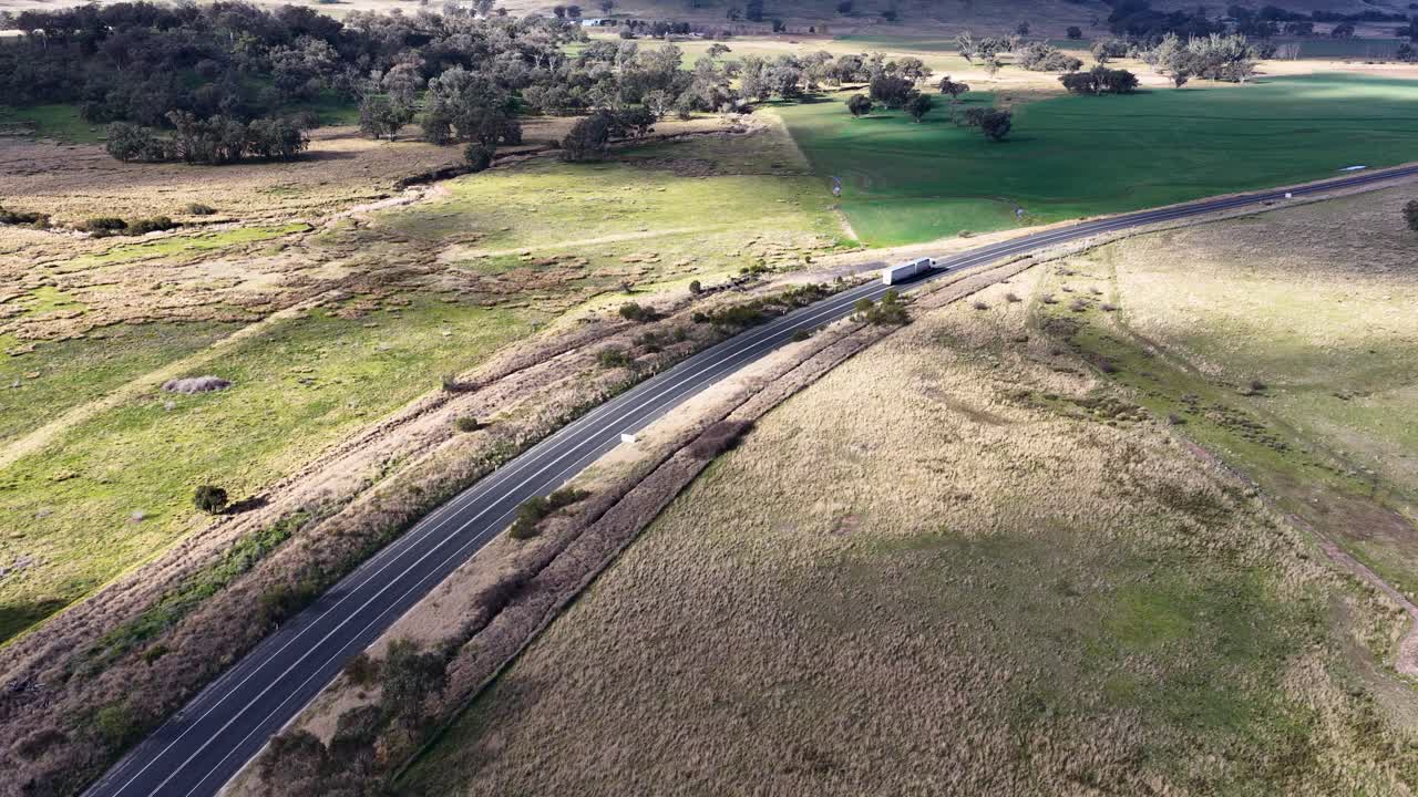 Aerial footage follows a semi truck traveling on a winding rural road through open countryside near Coonabarabran, New South Wales, under natural daylight
