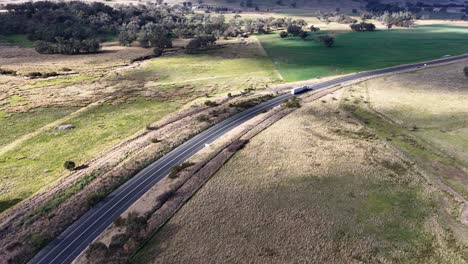 aerial footage follows a semi truck traveling on a winding rural road through open countryside near coonabarabran, new south wales, under natural daylight