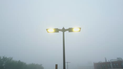 el avión no tripulado se eleva y se inclina hacia abajo a lo largo de las lámparas del estacionamiento con una cálida luz amarilla en la espesa niebla de la mañana brumosa