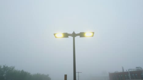 drone rises and tilts down along parking lot lamps with warm yellow light on thick fog misty morning