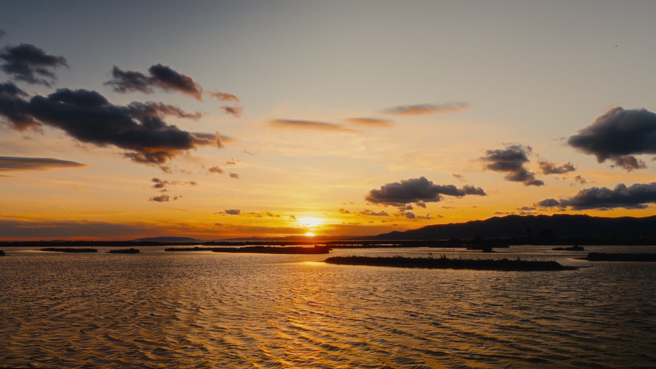 4K golden hour sun setting over lightly rippling waves of the delta, around small islands, low mountains in background.