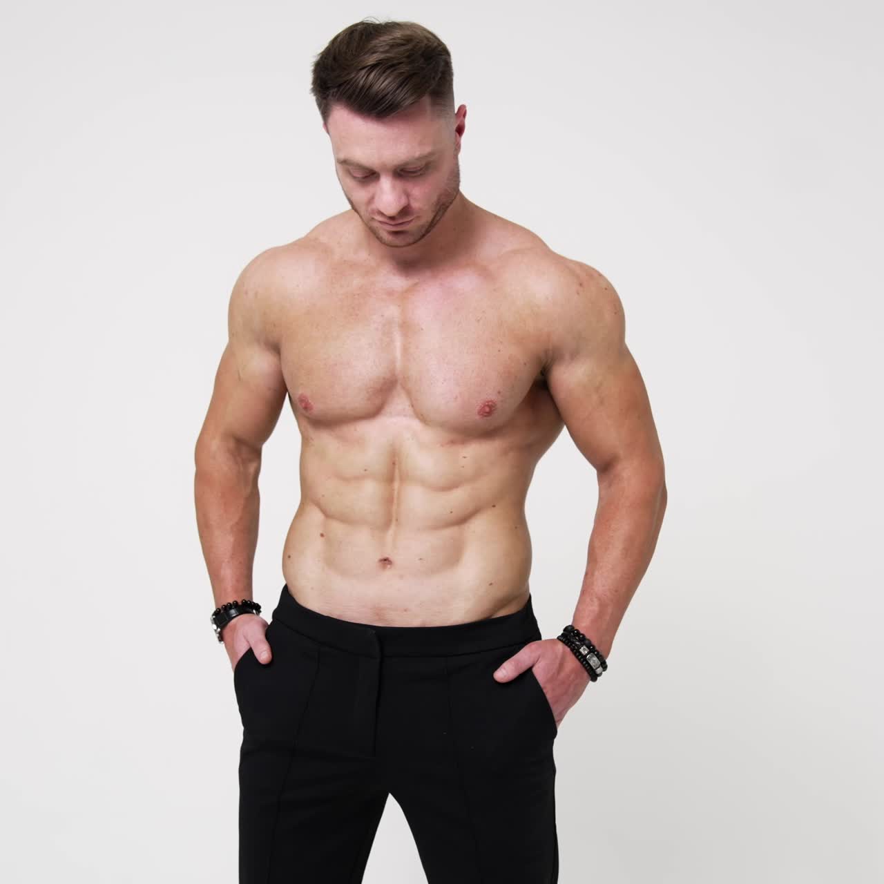 Uomo caucasico muscoloso e forte, a torso nudo e in pantaloni neri. Uomo atletico che incrocia le mani sul petto e guarda la fotocamera. Sfondo bianco.