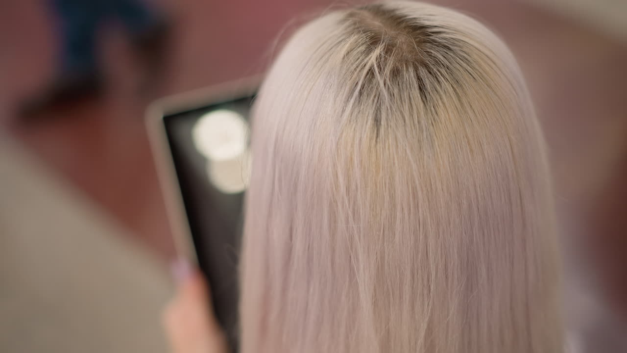 back view graceful lady with long hair seated on bench in modern mall tapping tablet screen with manicured nails, blurred display and soft indoor lighting creating serene digital moment