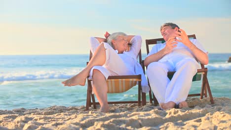 elderly couple sitting in deckchairs on a beach