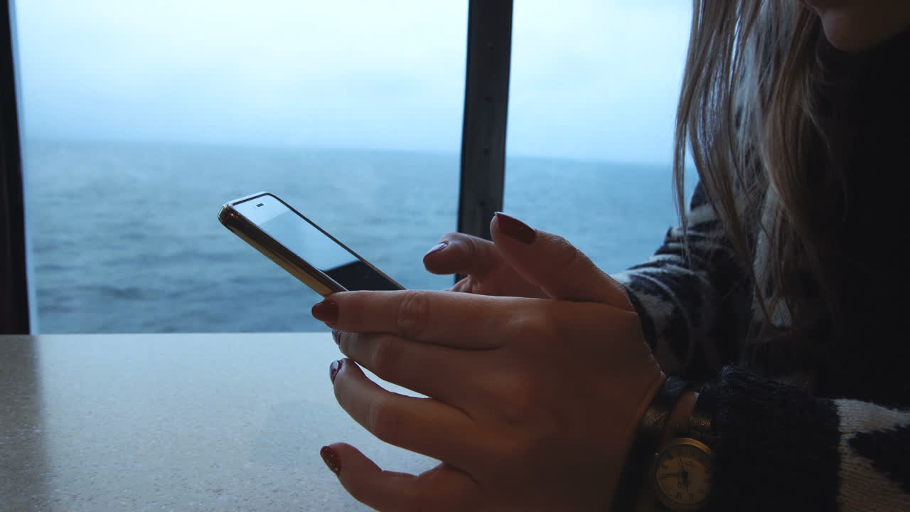 Person using a smartphone with an ocean view from a window on a ship