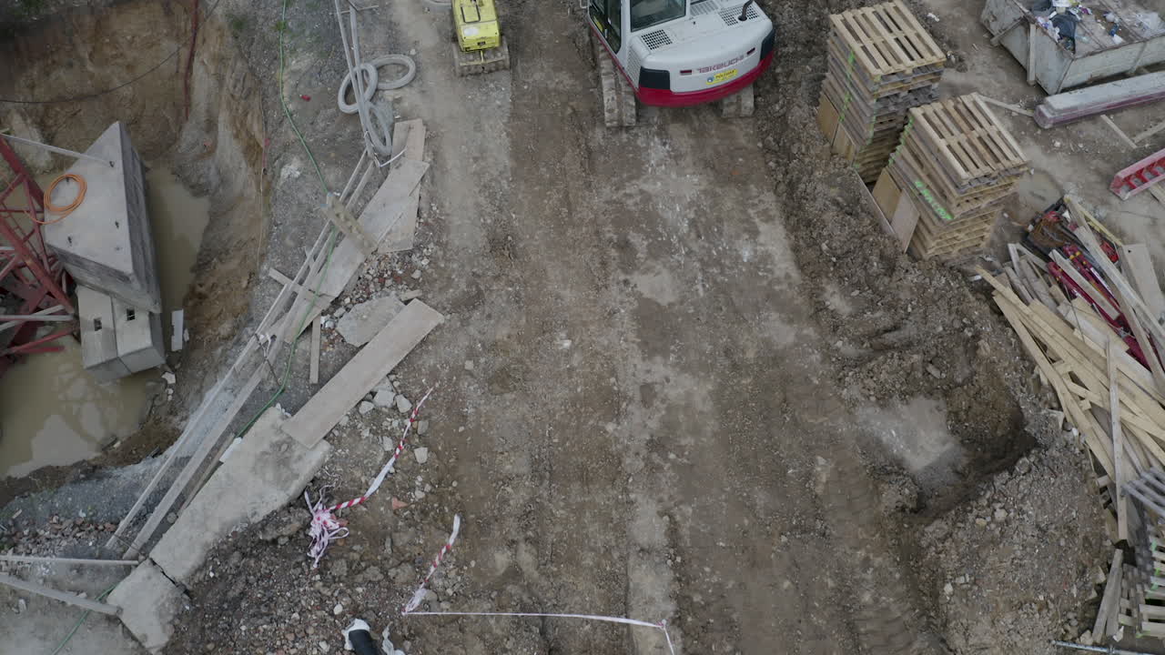 trabajador caminando frente a una excavadora en un sitio de construcción, tiro cenital