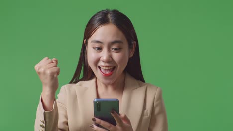 행복한 아시아 사업가 여성이 스튜디오에서 녹색 화면에서 스마트폰을 사용하는 동안 축하합니다.