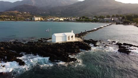 Weiße-Kapelle-Mit-Griechischer-Flagge-In-Georgiopoli,-Kreta,-Luftaufnahme