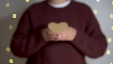 mujer ofrece un corazón con luces de navidad de fondo