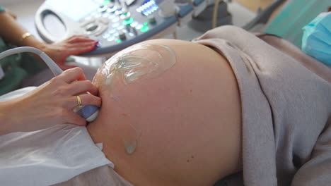 woman at ultrasound examination. big pregnant belly with applied gel and doctor's hand with device for ultrasonic check up.