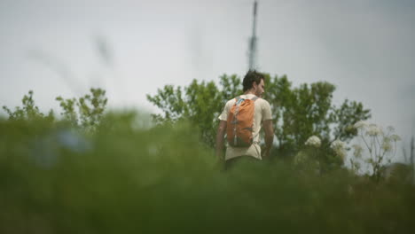 Excursionista-Con-Una-Mochila-Naranja-Caminando-Hacia-La-Torre-De-Radio-En-La-Montaña-Slavnik,-Cámara-Detrás-De-La-Vegetación-En-Perspectiva-Baja