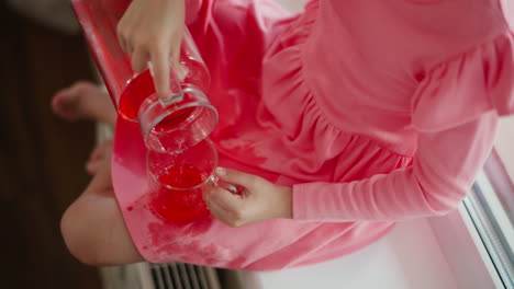 child pouring red liquid into cup, spilling on pink dress