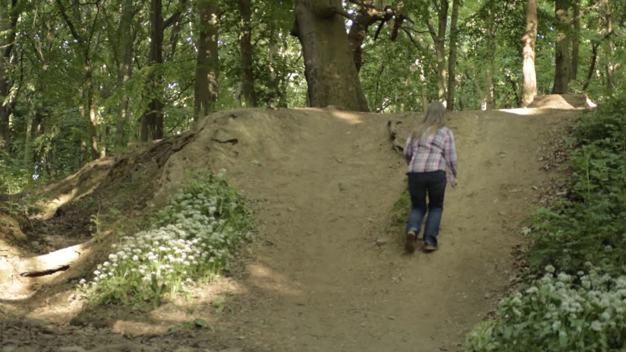 Woman running up hill in woodland countryside medium shot