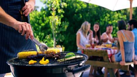 Mid-section-of-man-grilling-corn,-meat-and-vegetable-on-barbecue