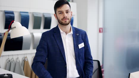 Portrait-of-young-car-salesman-at-dealership-salon,-looking-at-camera